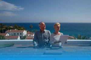 Older couple inspecting shifted terracotta roof tiles after a storm at a white house on the Spanish coast